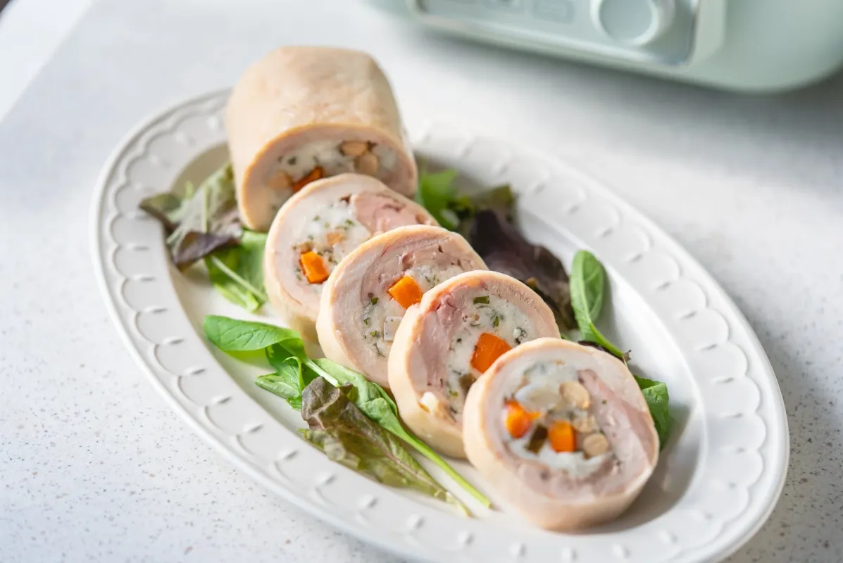 白い皿に盛り付けられた、鶏肉で野菜などを巻いたロールチキン