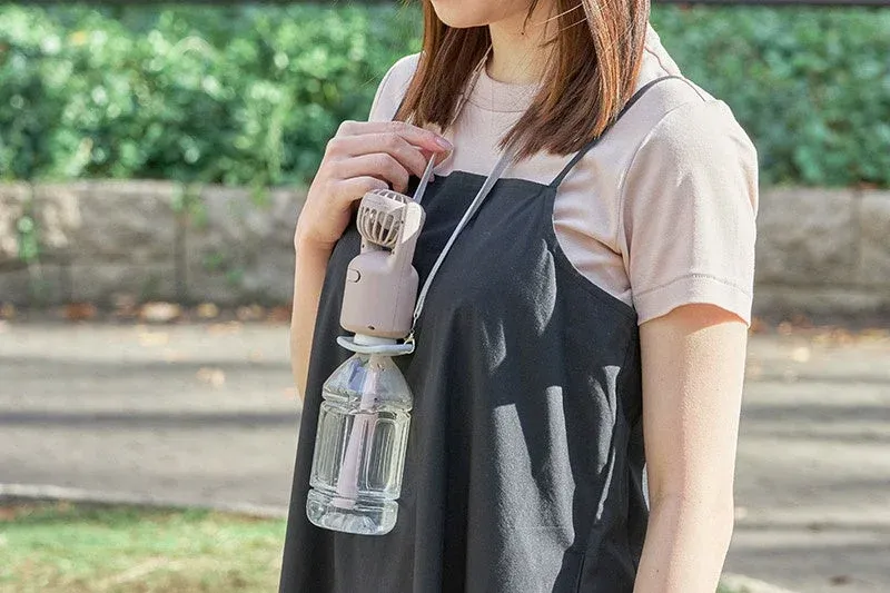 女性が首からポータブルミストファンを下げている様子を捉えた画像です。ファンはペットボトルに取り付けられており、夏の暑さ対策や熱中症予防に役立つ携帯型冷却グッズとして使用されていると見られます。