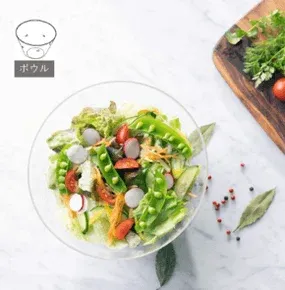 透明なボウルに入った色鮮やかなサラダの画像です。レタス、スナップエンドウ、ミニトマト、きゅうり、ラディッシュなど様々な野菜が含まれており、健康的で新鮮な印象を与えます。