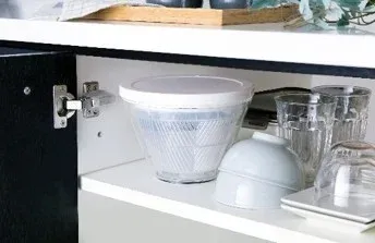 開いたキッチンの収納棚に、サラダスピナー、グラス、ボウルなどの食器が整理されて置かれている様子。清潔感のある収納空間を示唆しています。