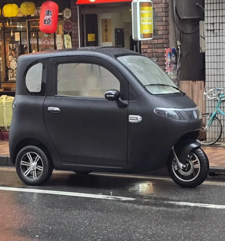 雨上がりの日本の街角に駐車された、黒いユニークな三輪自動車