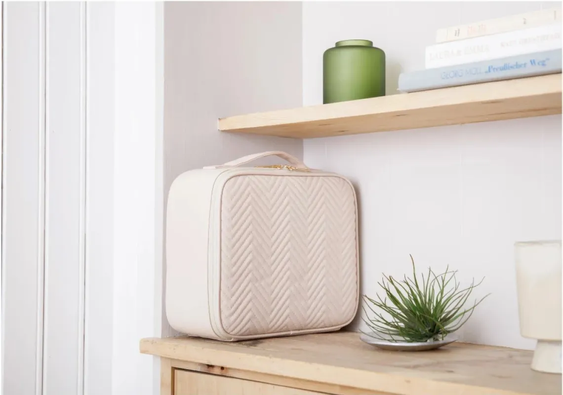 ベージュのバニティケースが木製の棚に置かれ、本や植物と調和している。